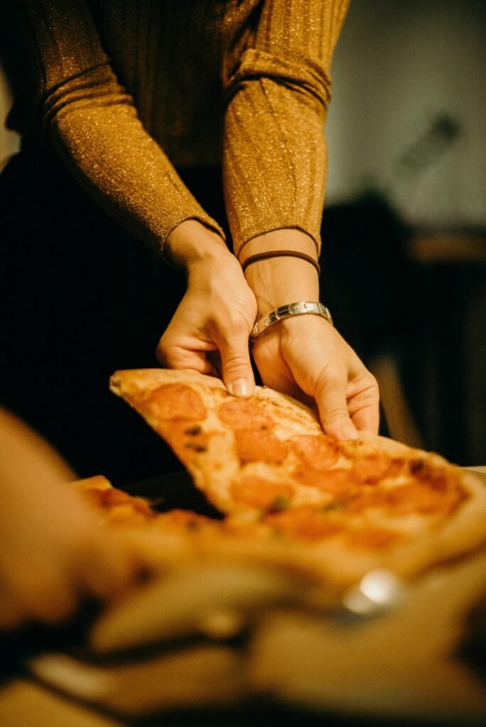Close-up of hands serving a pepperoni pizza slice indoors, warm and inviting.